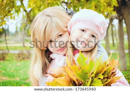 Autumn portrait of two little pretty happy girls with maple leaves in autumn park. Adorable girls in trendy wear posing outdoors on beautiful autumn day