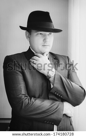 Gangster look. Handsome man with hat wearing dark suit. Retro fashion fifties young businessman. Black and white photo.