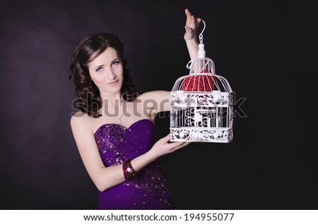 Beautiful fashionable woman holding cell in studio. Fashion portrait of young sexy alluring woman girl in elegant evening lilac dress posing on black background