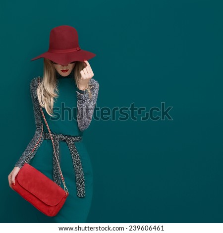 Lovely Blond model in fashionable red Hat and a red Clutch on green background