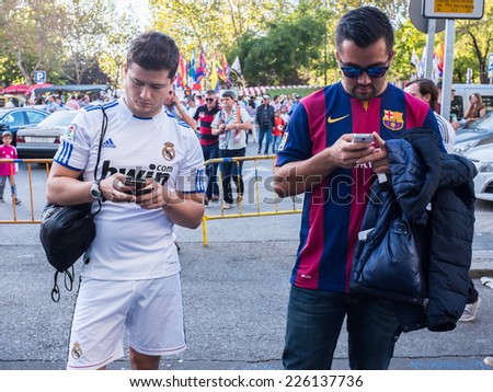 MADRID, SPAIN - OCTOBER 25, 2014: A couple of friends supporting Real Madrid and Barcelona watching their Smartphones at Santiago Bernabeu Stadium Gates before the Real Madrid-Barcelona match.