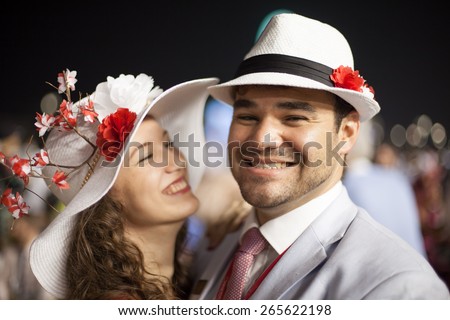 young beautiful couple smiling and laughing while wearing flower hats at the Dubai World Cup Horse Race