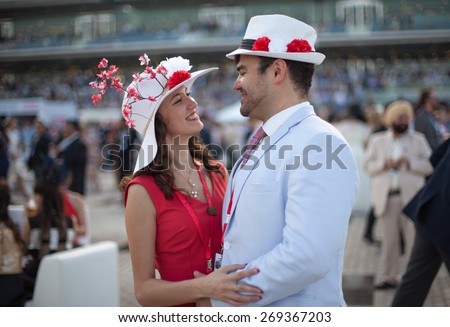 young beautiful couple smiling and laughing while wearing flower hats at the Dubai World Cup Horse Race
