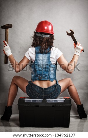 Sex equality and feminism. Back of sexy girl sitting on toolbox and holding wrench spanner and hammer tools on gray. Young attractive woman working as construction worker. Studio shot.