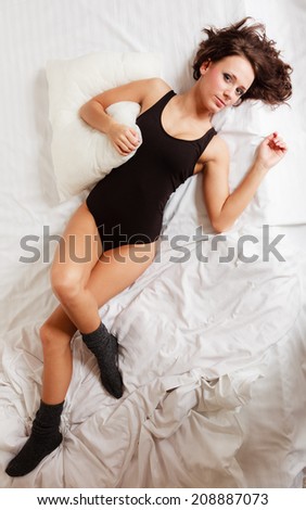 Sexy lazy girl in black body hugging a pillow on the bed. Young attractive woman lying lazing in bedroom at morning.