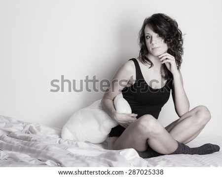 Sexy lazy pensive girl in black body hugging a pillow on the bed. Thoughtful attractive woman relaxing lazing in her bedroom.