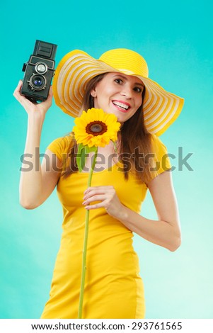 summer woman wearing yellow dress and hat with sunflower and old vintage camera in hand on vivid blue background