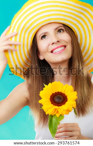 Closeup portrait of attractive summer woman in yellow hat with sunflower in hand on blue background