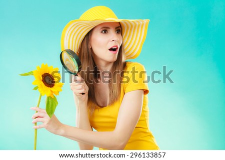 Botanist woman funny face expression in yellow hat examining flower looking through magnifying glass on blue background
