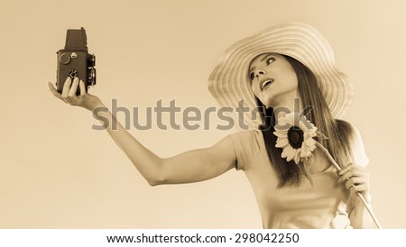 summer woman wearing yellow hat with sunflower taking self picture with old vintage camera sepia filter