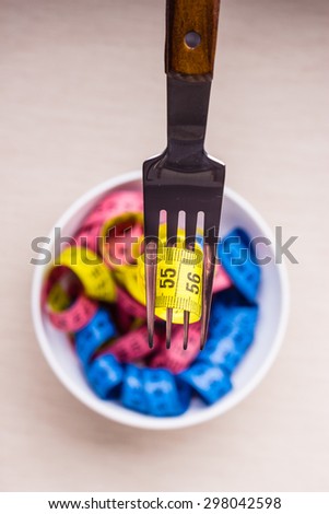 Diet food healthy lifestyle and slim body concept. Many colorful measuring tapes in bowl on table with fork, top view
