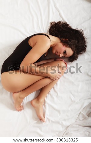 Sad unhappy girl in black body lying in fetal position on bed. Young lonely woman relaxing lazing in bedroom. Depression.