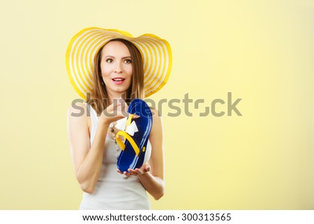 Holidays summer fashion concept. Woman in big yellow hat holding flip flops in hand bright background.