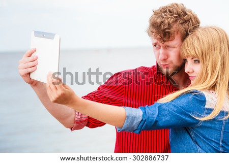 Technology holidays and happiness concept. Young couple taking self picture selfie with tablet outdoor on by seaside