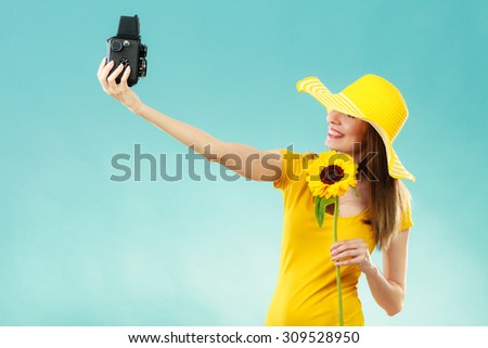 Summer woman wearing yellow dress and hat with sunflower taking self picture with old vintage camera on blue background