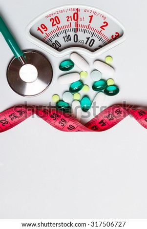 Healthy eating, medicine, health care, food supplements and weight loss concept. Pills with measuring tape and stethoscope on white scales