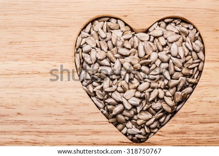 Whole food. Heart shaped sunflower seeds on wood surface background