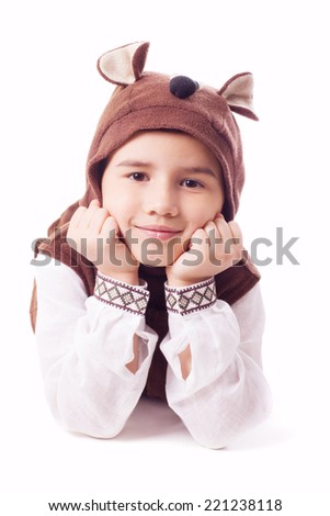 Playful boy wearing in a bear costume lies on a floor and holding head up with hands on face