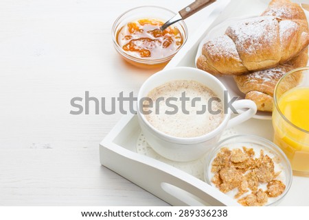 French breakfast with croissants, apricot jam, coffee, orange juice and natural yogurt with cornflakes served on white wooden table