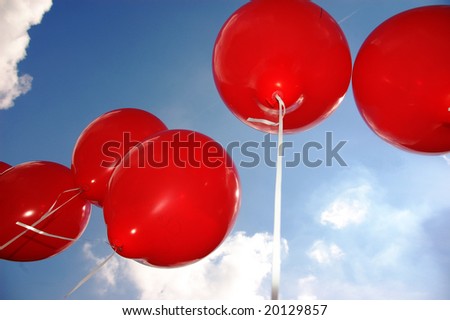 Flying red balloons under a blue sky with clouds