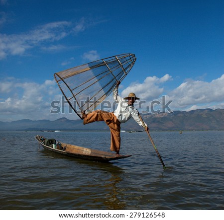 TAUNGGYI, SHAN, MAYANMAR - December, 06, 2014:  A local fisherman balances on his canoe, holding his net high and his oar in the water.