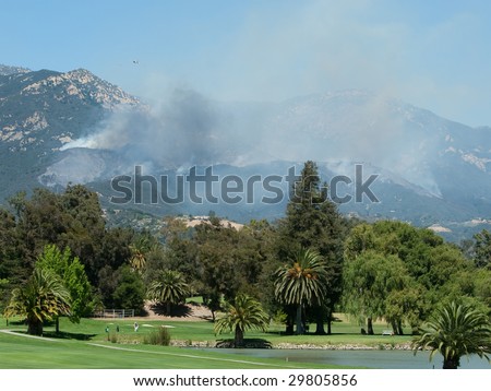 SANTA BARBARA, CA - MAY 06 : A fixed wing fire suppressant plane flies over the Jesusita Fire, while golfers play in the foreground May 06, 2009 in Santa Barbara, CA.