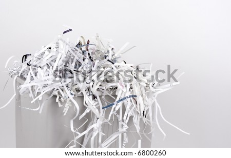An office shredder overflows with shredded paper.