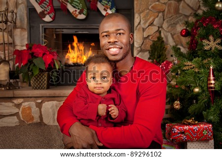 Happy Black Father and Son in front of Fireplace Decorated with Christmas Tree