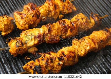 Indian chicken tikka kebabs, marinated in spices and yogurt, cooking on griddle plate. Shallow DoF, focus on centre.