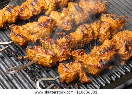 Indian lamb tikka kebabs cooking on hot griddle plate. Shallow DoF, focus on centre.