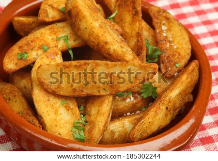 Spicy potato wedges in terracotta dish.