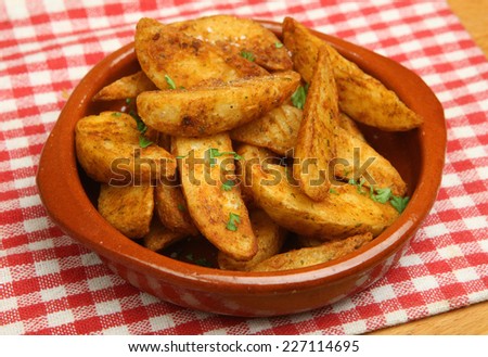 Spicy potato wedges in a terracotta dish.