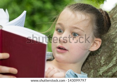 A young girl showing emotion whilst reading a book.