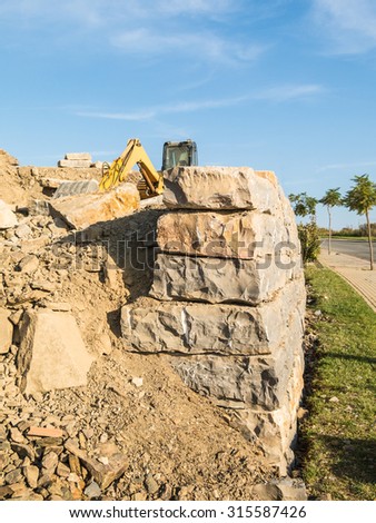 The end view of a partially constructed large limestone wall with a yellow digger in the background.
