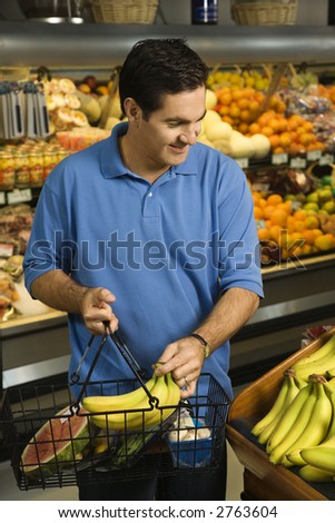 Caucasian mid-adult male grocery shopping for bananas.