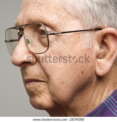 Close-up profile portrait of Caucasian elderly man with glasses and hearing aid.