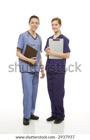 Portrait of Caucasian women doctors in medical scrubs standing holding medical charts against white background.