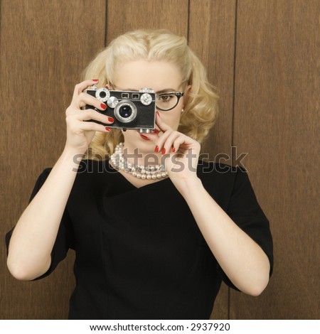 Mid-adult Caucasian female in vintage outfit holding a vintage film camera up to her face.