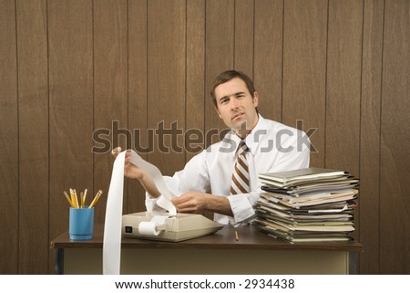 Mid-adult Caucasian male holding printout from calculator in office setting.