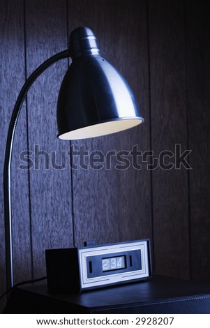 Dim desk lamp and retro clock against wood paneling at night.