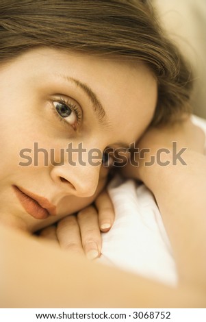 Head shot of nude Caucasian mid-adult woman lying down with head on hands.