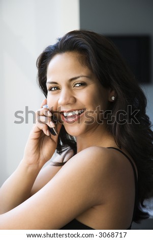 Hispanic young adult woman looking at viewer and talking on cell phone.