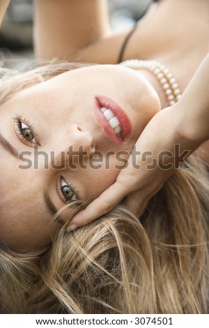 Close-up portrait of Caucasian young adult woman lying with hand to face making eye contact.