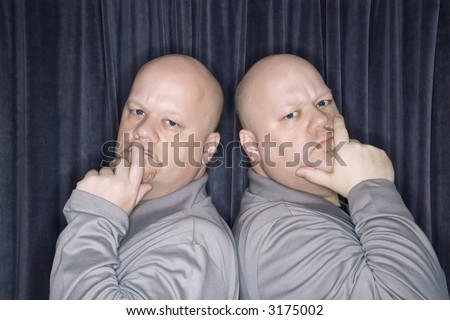 Caucasian bald identical twin men standing back to back and looking at viewer with hands to mouth.