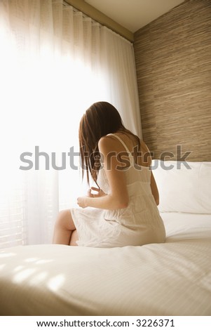 Pretty young Caucasian woman sitting on bed wearing nightgown.