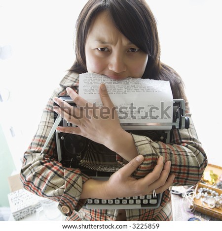 Pretty young Asian woman holding typewriter and biting page.