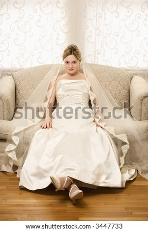 Caucasian bride slouching in love seat.
