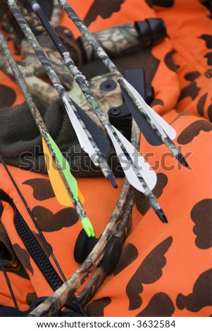 Still life shot of bow and arrows laying against blaze orange camouflage.