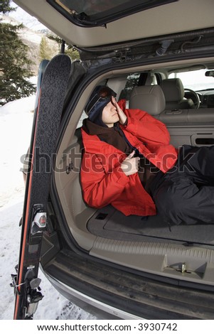 Caucasian teenager sleeping in back of SUV with ski gear.