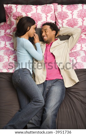 African American couple laying on bed looking at each other.